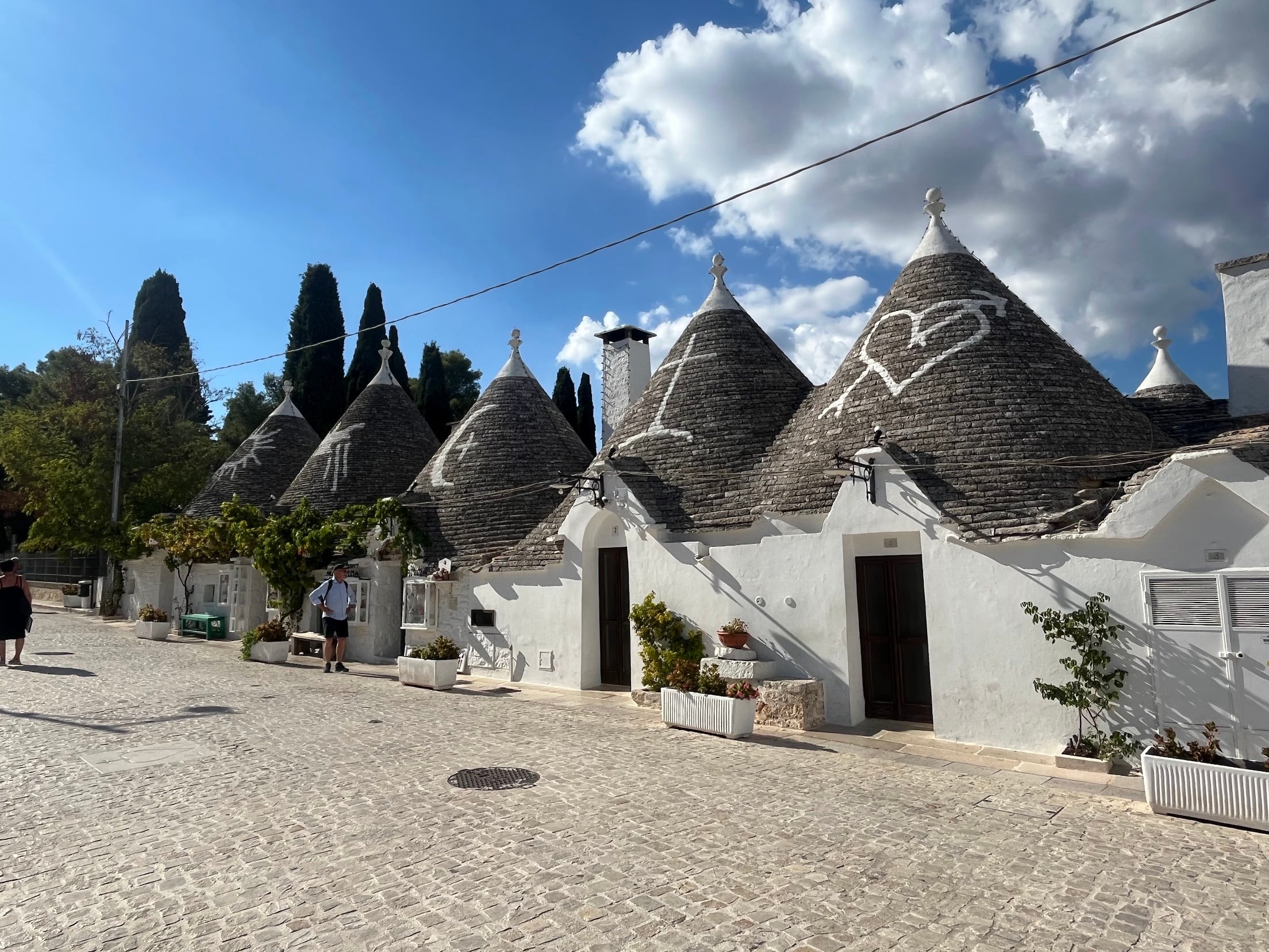 A row of trulli in Alberobello with conical stone roofs, several painted with white symbols